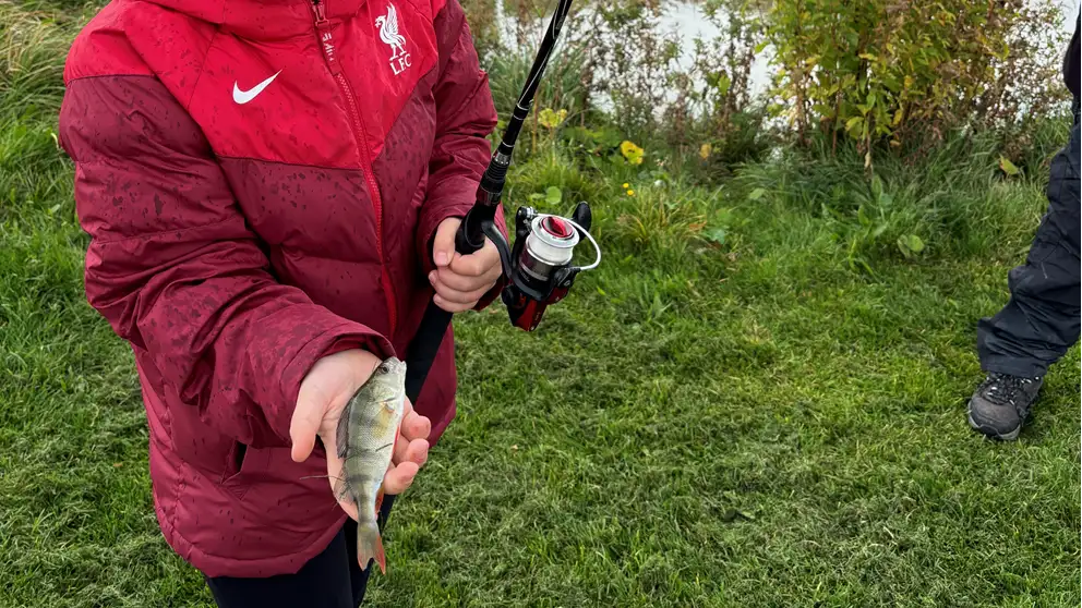 Barn med fiskestang og en fisk i hånden