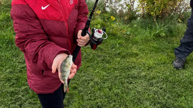 Barn med fiskestang og en fisk i hånden
