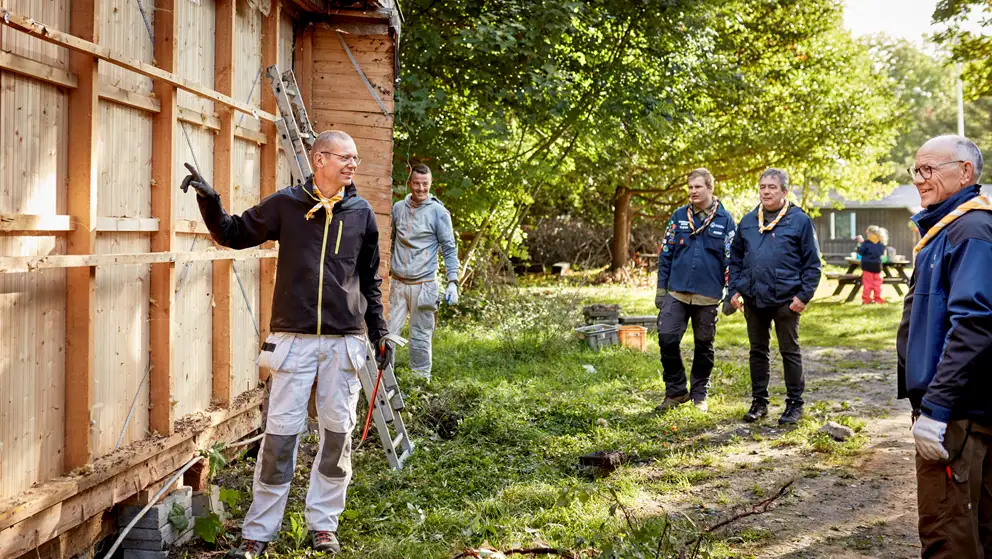 Håndværker peger forklarende på spejderhytte, der er ved at blive renoveret