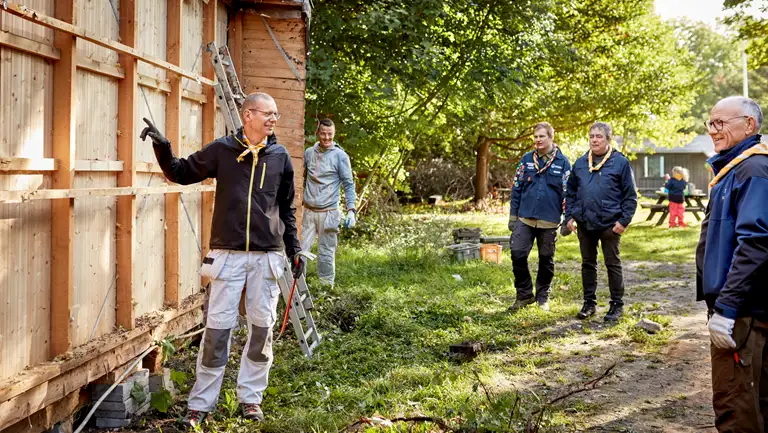 Håndværker peger forklarende på en spejderhytte, der er ved at blive renoveret