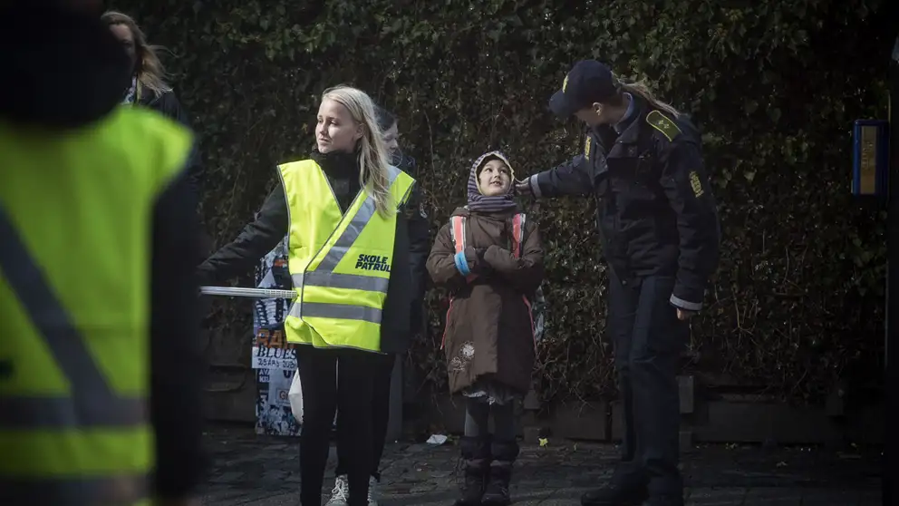 Billede af to børn, der er skolepatrulje og hjælper børn over vejen sammen med en kvindelig politibetjent.