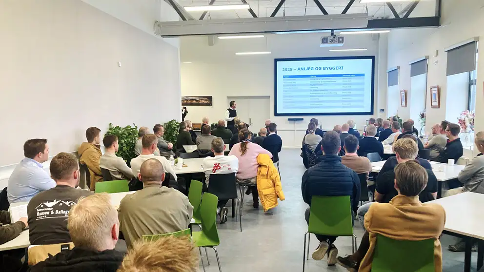 Billede af mennesker i en sal, der sidder ved borde og ser en præsentation