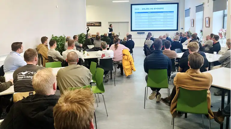 Billede af mennesker i en sal, der sidder ved borde og ser en præsentation