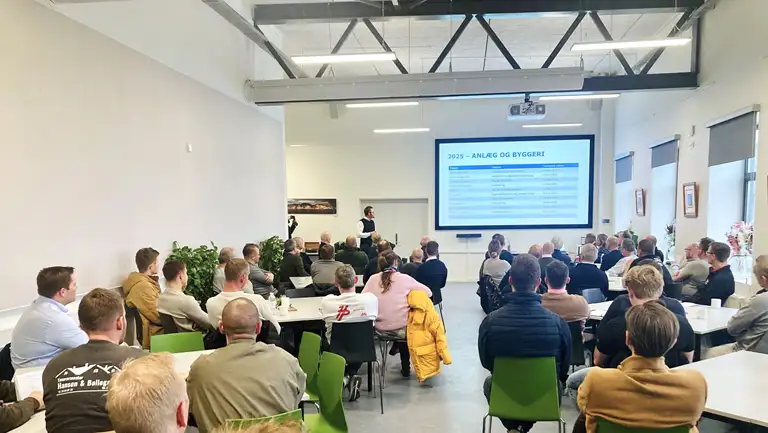 Billede af mennesker til håndværkermøde, der sidder ved borde og ser en præsentation