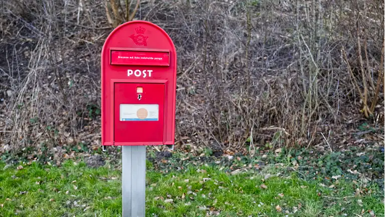 Billede af en rød postkasse, der står frit i en vejkant