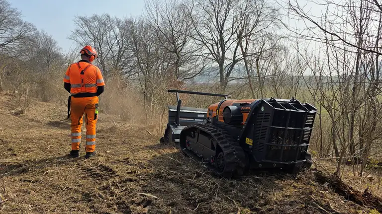 Arbejdsmand manøvrerer robotknuser i terræn